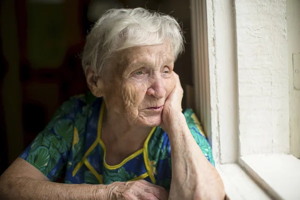 Elderly lady looking out window. — Stock Photo, Image