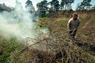Yaşlı kadın çiftliğinde dalları temizler ve yakar..