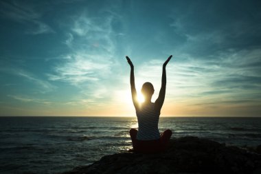 Silhouette of woman practicing yoga on the beach at sunset.	