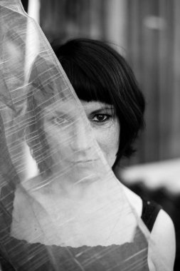 Kadın açık havada, yüzünün yarısı şeffaf peçeyle kaplanmış. Siyah beyaz fotoğraf.