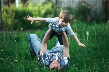 Genç baba ve küçük oğlu yaz parkında çimlerde oynuyorlar..