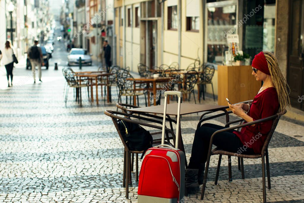 Woman with red suitcase sitting at a table at an outdoor cafe.