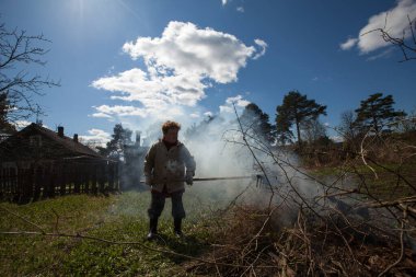 Yaşlı kadın köydeki çiftliğinin yakınındaki evin dallarını yakıyor..