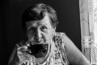 Yaşlı bir kadın evinde bir masada oturuyor. Siyah beyaz fotoğraf.