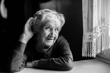 Duyma zorluğu çeken yaşlı bir kadın elini kulağına dayar. Siyah beyaz fotoğraf.