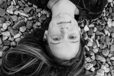 Nehir çakıl taşlarının üzerinde yatan genç kız, en üstteki yakın plan portresi. Siyah beyaz fotoğraf.