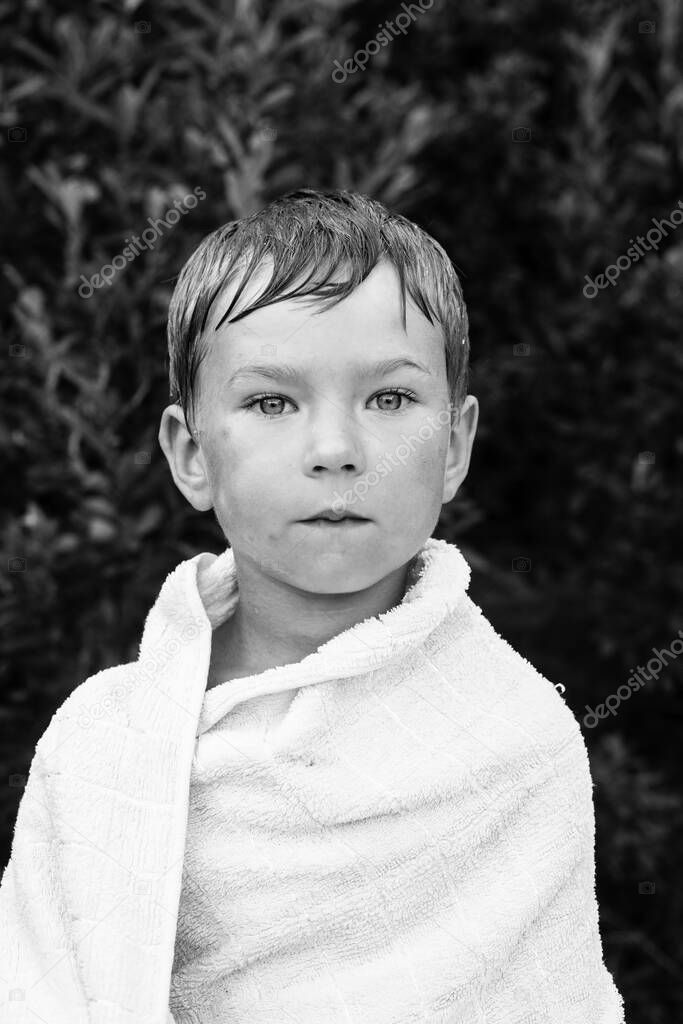 Portrait of little boy wrapped in a towel after bathing outdoors. Black and white photo.