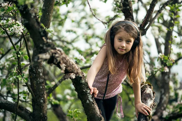 Liten Flicka Med Hörlurar Grenarna Ett Blommande Äppelträd — Stockfoto