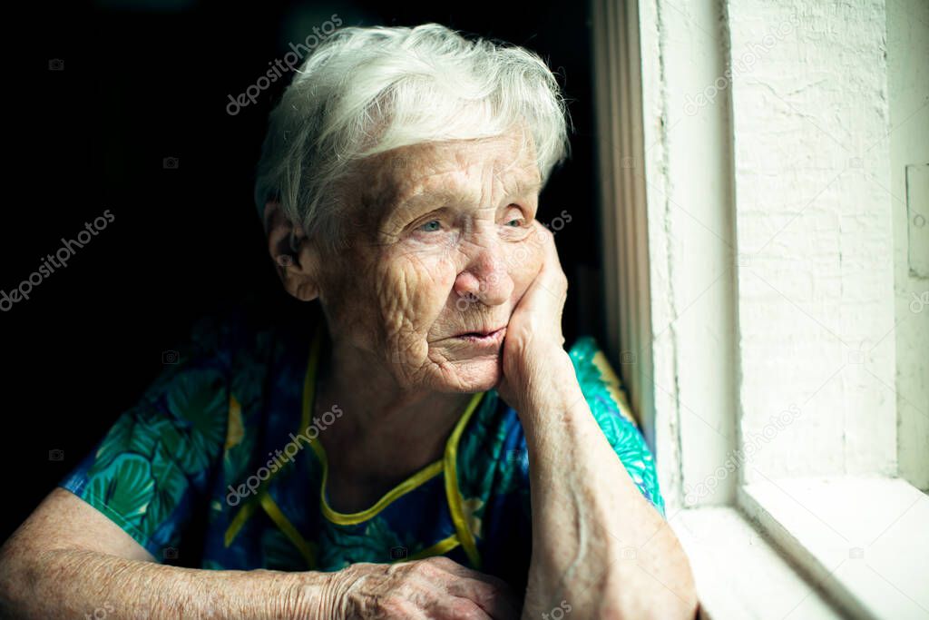 The old woman looks out the window with displeasure.