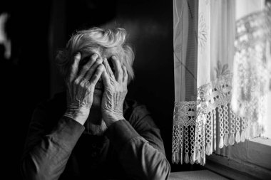 Yaşlı bir kadın iki eliyle yüzünü kapattı. Siyah beyaz fotoğraf.