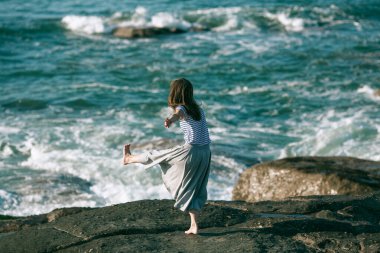 Bir kadın okyanus kıyısında dans ve koreografi ile meşgul..