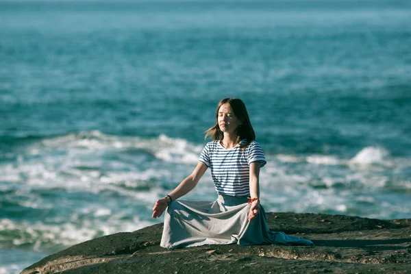 若いヨガの女性は大西洋岸の岩の上に座って蓮の位置で瞑想します — ストック写真