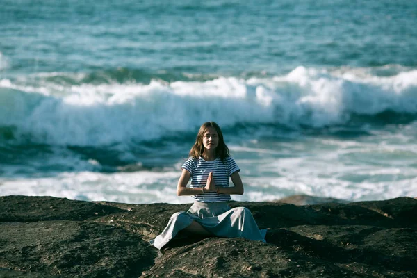 美丽的年轻瑜伽女子坐在美丽海岸的岩石上 以荷花的姿态沉思着 — 图库照片