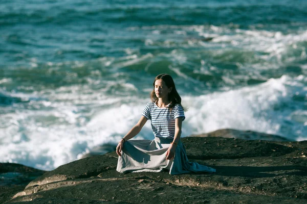 ヨガの女性は海の海岸の岩の上に座って蓮の位置で瞑想 — ストック写真