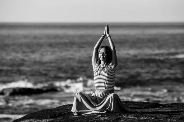 若いヨガの女性は 大西洋岸の岩の上に座って蓮の位置に瞑想します 白黒写真 — ストック写真
