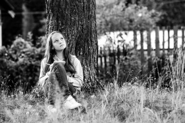 Kız öğrenci parkta otururken bir mandıra defterine yazı yazıyor. Siyah beyaz fotoğraf.