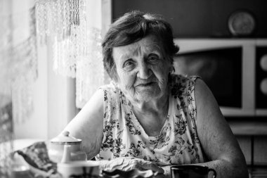 Yaşlı kadın emekli, evinde bir masada oturuyor. Siyah beyaz fotoğraf.