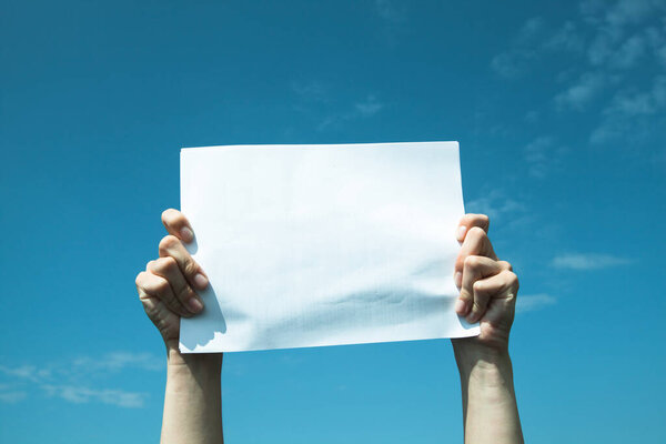 Руки держат чистый лист белой бумаги над небом.