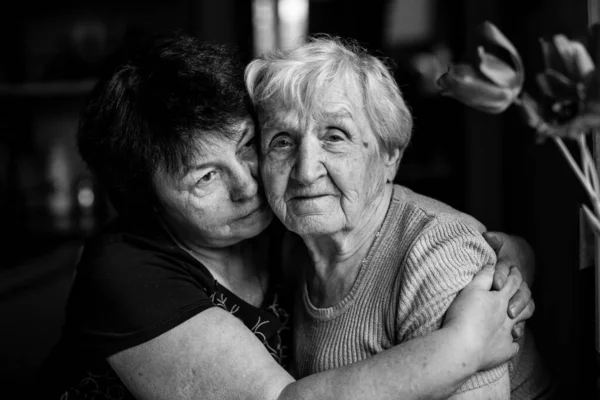 Portrait of an old woman embrace with her adult daughter. Black and white photo.