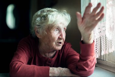 Yaşlı bir kadın duygusal olarak konuşuyor. Evde bir masada oturuyor..