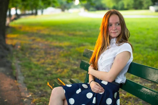 Altın gün batımında parkta oturan uzun saçlı genç kız..