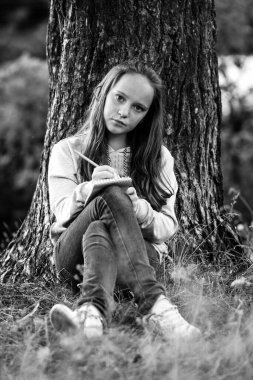 Parkta otururken deftere yazan kız. Siyah beyaz fotoğraf.