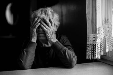 Yaşlı kadın yüzünü kırışık ellerle örtüyor. Siyah beyaz fotoğraf.