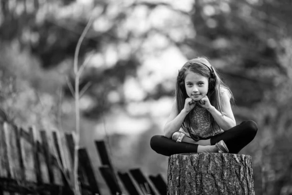 一个戴耳机的可爱小女孩坐在村子里的树桩上 黑白照片 — 图库照片#