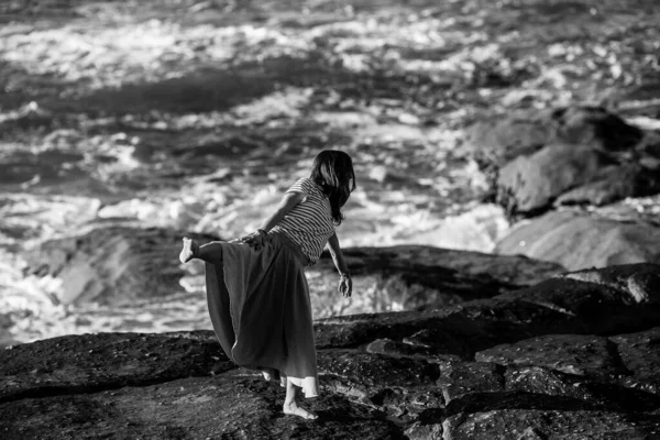 Dance woman is engaged in choreography on the ocean coast. Black and white photo.