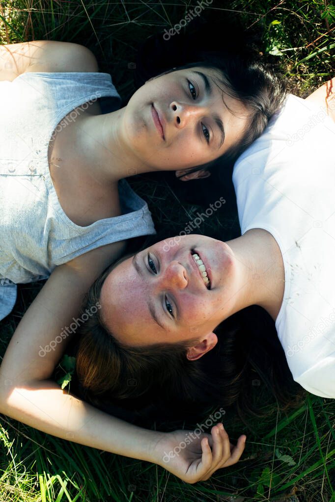 Top view portrait of two young girl lying on grass having good time. 