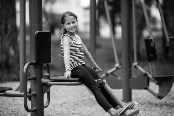 屋外の公共のトレーナーマシンに座っている少女 白黒写真 — ストック写真