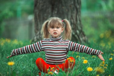 Küçük şirin kız yeşil çimenlerde oturuyor ve pişmanlıkla ellerini kaldırıyor..