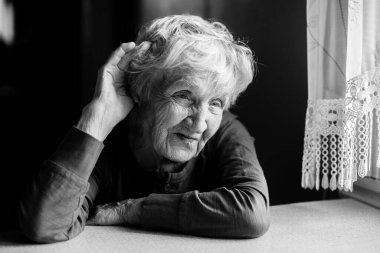 Duyma zorluğu çeken yaşlı kadın elini kulağına koydu. Siyah beyaz fotoğraf.