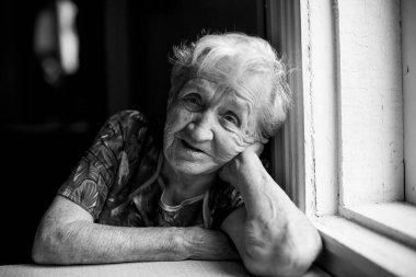 Pencerenin yanında oturan yaşlı bir kadın. Siyah beyaz fotoğraf.
