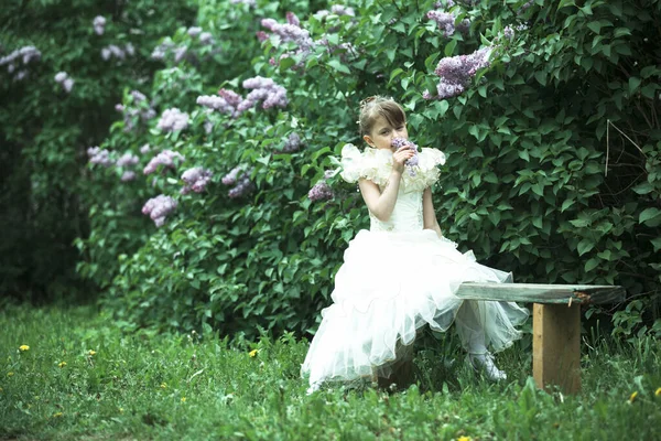 一个可爱的小女孩坐在长椅上 手里拿着一束鲜花 — 图库照片