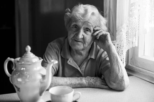 お茶を飲みながらテーブルに座っている老婆の肖像画 — ストック写真