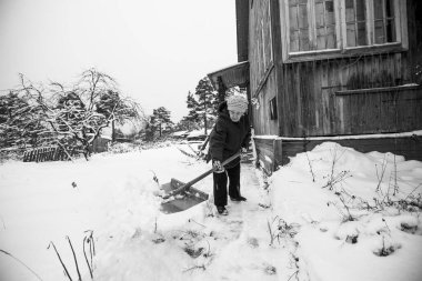 Yaşlı bir kadın köydeki evinin yakınındaki karı temizliyor. Siyah beyaz fotoğraf.