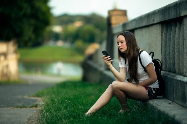 一个少女坐在街上 手里拿着智能手机 — 图库照片