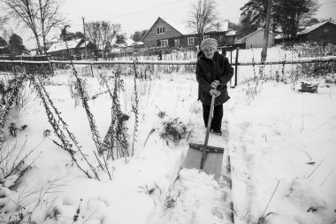 Yaşlı bir Rus kadın köydeki evinin yakınındaki karı temizliyor. Siyah beyaz fotoğraf.