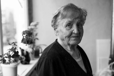 Pencerenin yanında yaşlı bir kadın. Siyah beyaz fotoğraf.