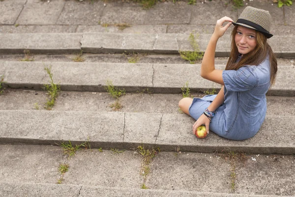 Jong meisje dragen van een hoed zittend op stenen trappen — Stockfoto