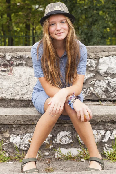 Chica joven con un sombrero sentado en escalones de piedra — Foto de Stock
