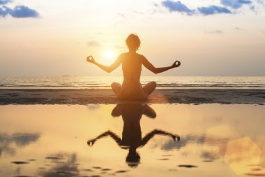 Kadın plajda yoga yapıyor.