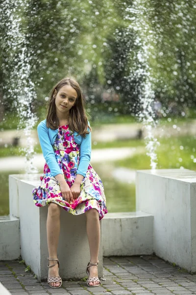Маленькая девочка сидит возле фонтана — стоковое фото