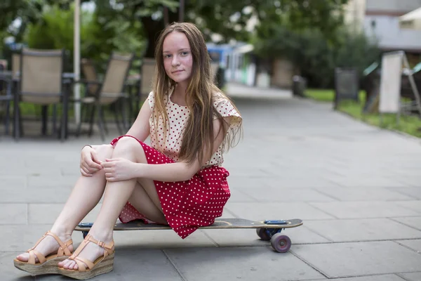 Милая девочка-подросток сидит на скейтборде — стоковое фото