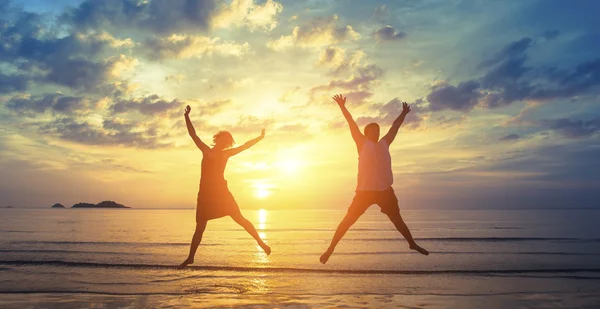 Silhouettes of happy young couple jumping — Stock Photo, Image