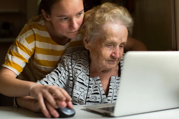 Chica enseña la abuela a trabajar en la computadora . —  Fotos de Stock