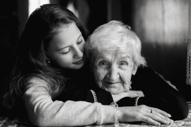Genç bir kızın siyah beyaz portresi. Yaşlı bir kadını kucaklıyor. Derin aile bağları, şefkat ve sessiz duyguları yumuşak doğal ışıkta gösteriyor..