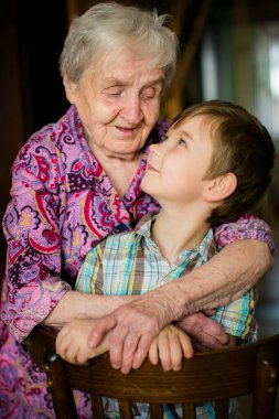 Genç torununa evde sarılan yaşlı kadın, sıcak bir yuva ortamında nesiller boyu sevgi, ilgi ve bağlarını gösteren duygusal aile portresi..