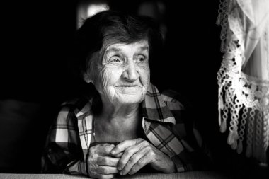 Pencerenin yanında oturan yaşlı bir kadının siyah beyaz portresi. Yumuşak doğal ışık ifade eden yüzünü ve ellerini ön plana çıkarıyor, samimi ve duygusal bir sahne yaratıyor..